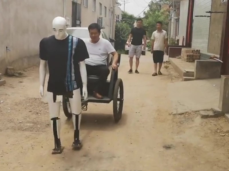 段男坐自己發明的拉車,由車夫機械人拉着在村内行走。(網圖)