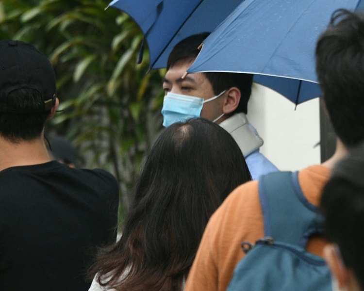 周健豪在多人撐傘下保護地離開法院。